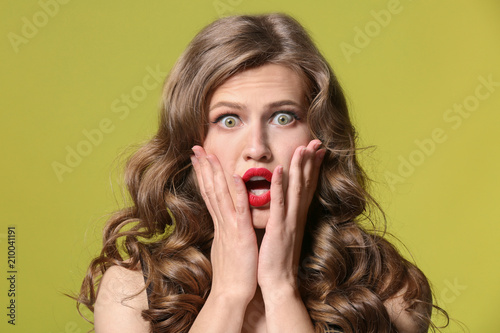Shocked young woman on color background