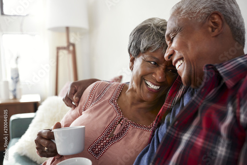 Loving Senior Couple Sitting On Sofa At Home Relaxing With Hot Drink