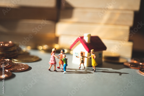 Miniature people, children playing at home around stack coins using as family and education concept