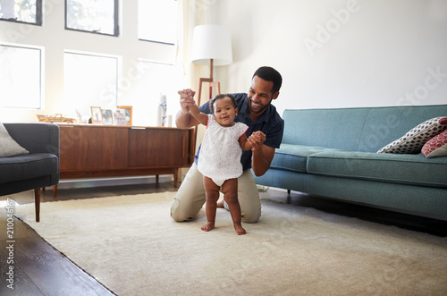 Father Encouraging Baby Daughter To Take First Steps At Home photo