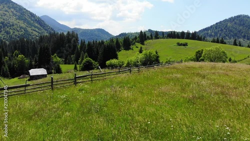 Panoramic view of idyllic mountain scenery with fresh green meadows in bloom on a beautiful sunny day in springtime. Aerial 4K view. Low air flight over mountain rural farm and meadow at sunny day photo