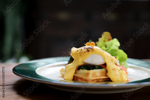 Breakfast food egg benedict , poached egg with yellow sauce with waffle and smoked salmon on wood background