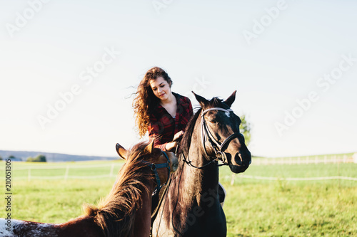 A girl sitting on a bay horse and the other horse approaching her.