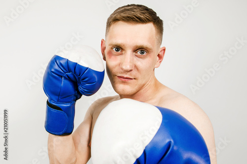 Young guy in blue boxing gloves on a light background. photo