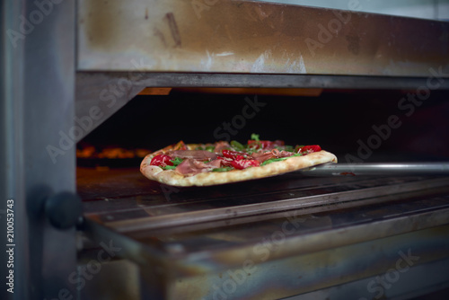 Cook putting Italian pizza to bake in oven