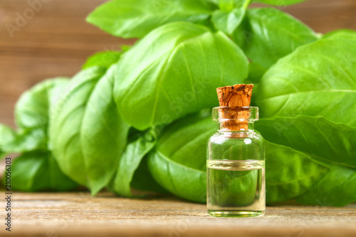 A bottle of basil essential oil with fresh basil leaves on a table.