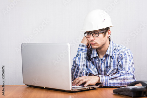 the guy in the white construction helmet works at the computer