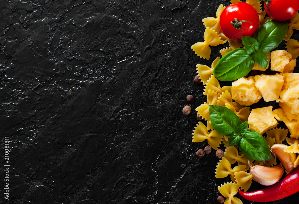 food background. Ingredients for cooking Italian pasta - farfalle pasta, red chili peppers, cherry tomato, basil, black pepper, garlic, parmesan cheese on dark background with copy space. top view