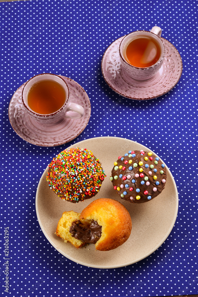 Baking with tea and chocolate on the table. Two cups of tea with cupcakes and chocolate with a multicolored powder on the table. Baking with tea and chocolate on the table. Two cups of tea with cupcakes and chocolate with a multicolored powder on the table.