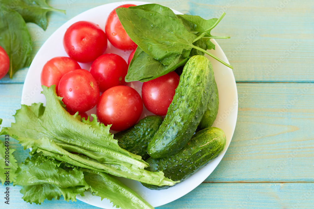 Tomatoes, cucumbers, spinach and lettuce leaves on a white plate. Tomatoes, cucumbers, spinach and lettuce leaves on a white plate.
