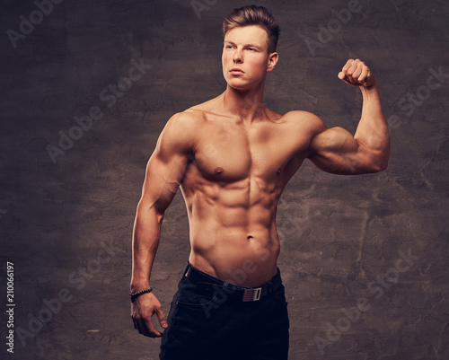 Strong shirtless young man model with nice muscular body showing his bicep at a studio.