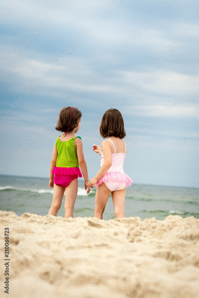 two little girls sisters are standing and showing themselves a shell on the beach in summer