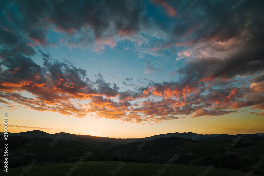 Beautiful dramatic sunrise in the mountains. Landscape with sunlight shining through orange clouds