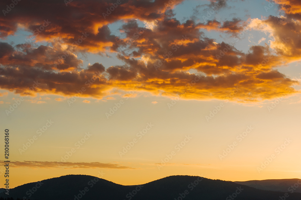 Beautiful dramatic sunrise in the mountains. Landscape with sunlight shining through orange clouds