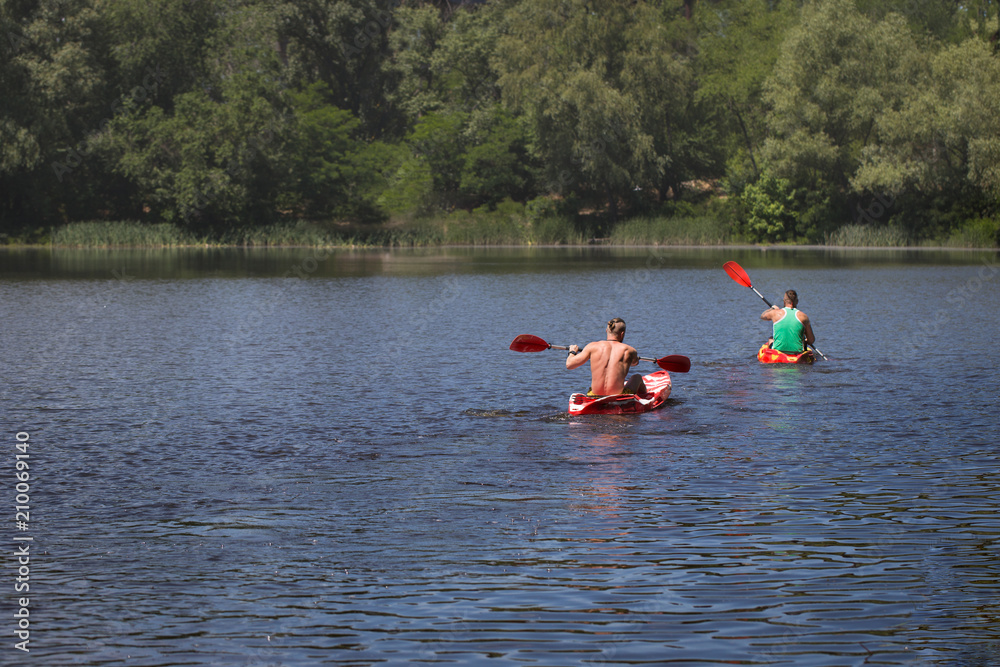 Young guys swim on kayaks along the river