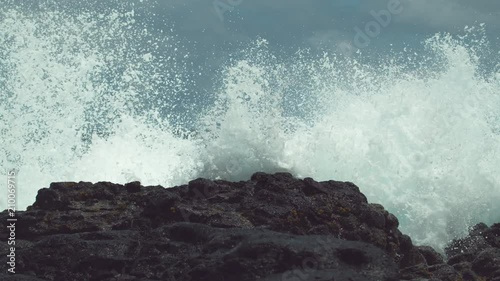 SLOW MOTION, CLOSE UP: Powerful ocean swell hits the tropical black rocky shore and splashes high in the air. Spectacular view of dangerous waves crashing into the tropical beach on Easter Island.