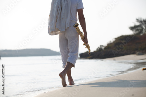 Мужчина с саксофоном идет по берегу моря