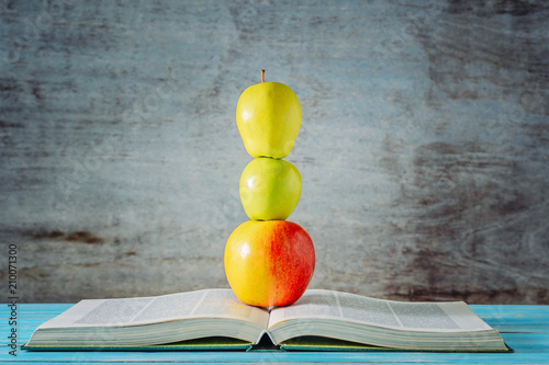 Open book and apples stacked in front of wooden background photo