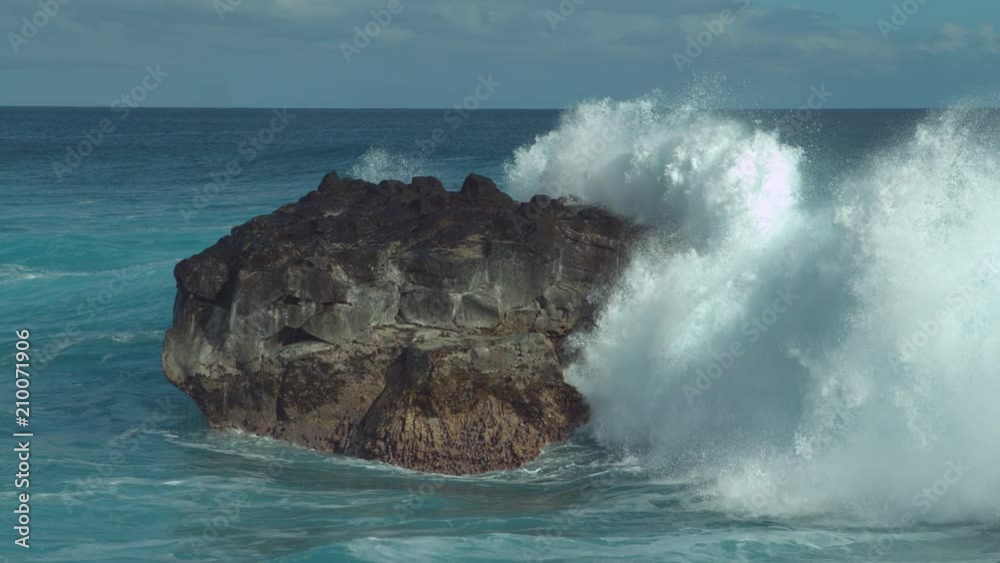 SLOW MOTION: Powerful ocean wave splashes across a big rock in the middle of the rough exotic sea. Breathtaking view of violent breaking wave foaming over a black rock near rocky tropical shore.