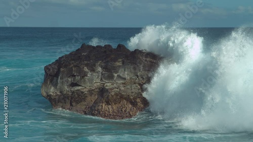 SLOW MOTION: Powerful ocean wave splashes across a big rock in the middle of the rough exotic sea. Breathtaking view of violent breaking wave foaming over a black rock near rocky tropical shore.