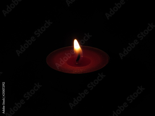 A small red tealight candle lit in a dark room on a table