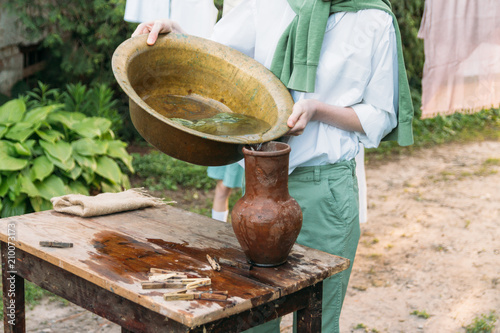 the boy holds a clay jug, pours water out of it into a copper basin. help photo