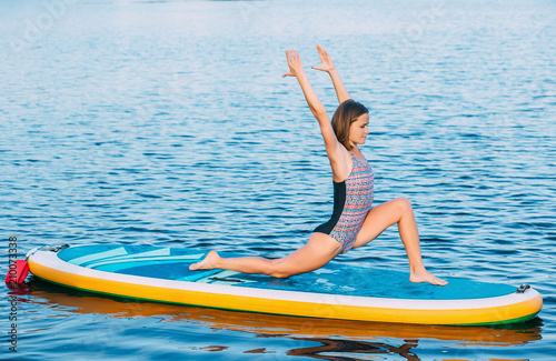 Pretty, sporty woman in yoga position on paddleboard, doing yoga on sup board at sea © Peakstock