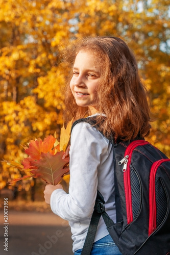 Portrait of a child girl  goes to school in the fall with a backpack and leaves in his hands.
