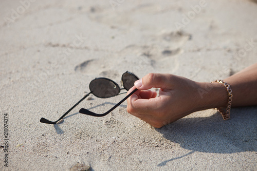 Мужчина лежит на песке и держит очки в руках. Саксофон на песке.