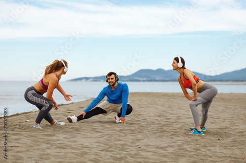 Group of young people is warming up before jogging on the beach by the sea
