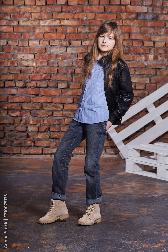 Beautiful stylish hipster girl ,looking camera,posing against rough brick wall. Attractive Adolescent woman wears casual fashionable clothes. Youth trend.Studio shot, loft interior.