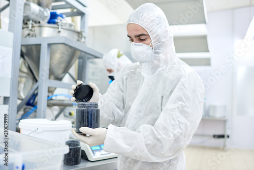 Production worker in protective clothing closing black jar with sports nutrition. photo