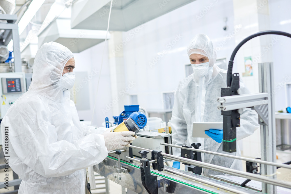 Production workers in protective clothing operating at conveyor belt holding ready package with sports nutrition. Production workers in protective clothing operating at conveyor belt holding ready package with sports nutrition.