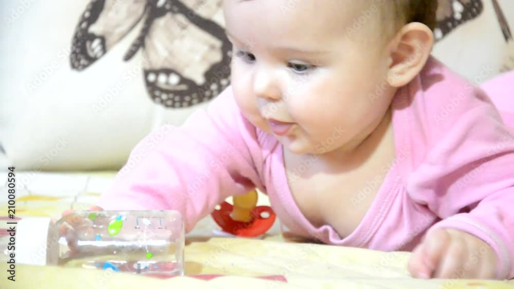 Cute baby girl showing tongue, the baby crawls on the couch, sucks a pacifier, a bottle, baby food, gets up from the hand, a child up to a year, todler Cute baby girl showing tongue, the baby crawls on the couch, sucks a pacifier, a bottle, baby food, gets up from the hand, a child up to a year, todler