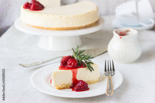 Classical vanilla cheesecake (New York cheesecake) with strawberry sauce and rosemary on white plate and light background