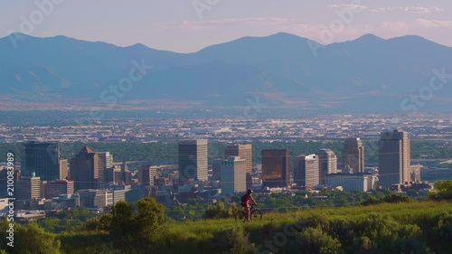 Mountain biker on a trail with dog following, overlooking Salt Lake City