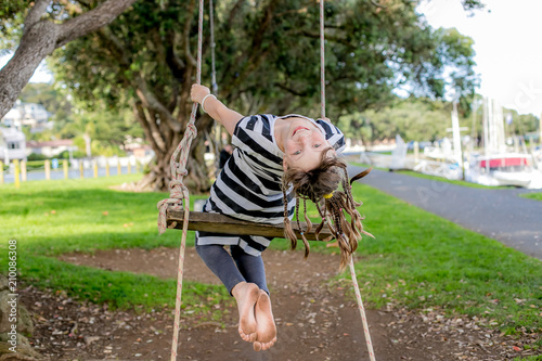 outdoor porrait of young happy child girl having fun on a rope swing, natural background photo