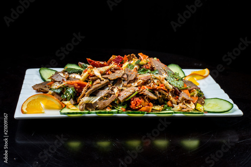 Chinese cuisine, boiled beef with cucumber and tomato in white plate, on black background photo