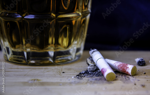 A cigarette with a woman's lipstick is placed with a glass of liquor.
