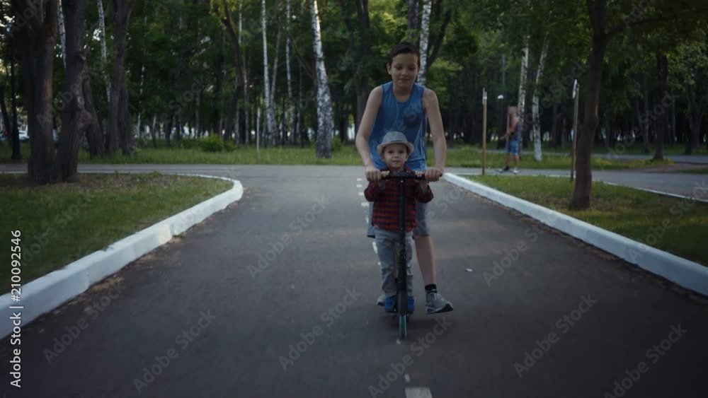 two brothers riding a kick scooter in a summer park. two brothers riding a kick scooter in a summer park.