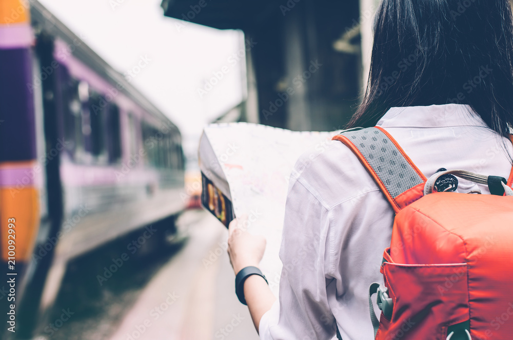 Girl wearing backpack holding map, waiting for a train. Traveling in Bangkok Thailand. Travel concept