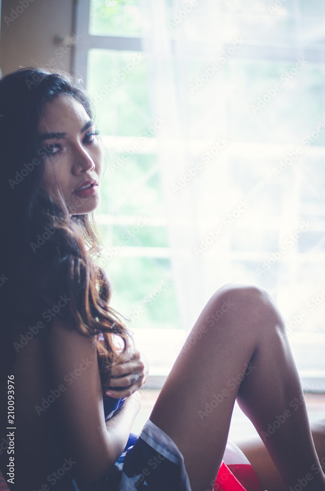 Fototapeta premium Young woman at home sitting on modern chair in front of window relaxing in her living room
