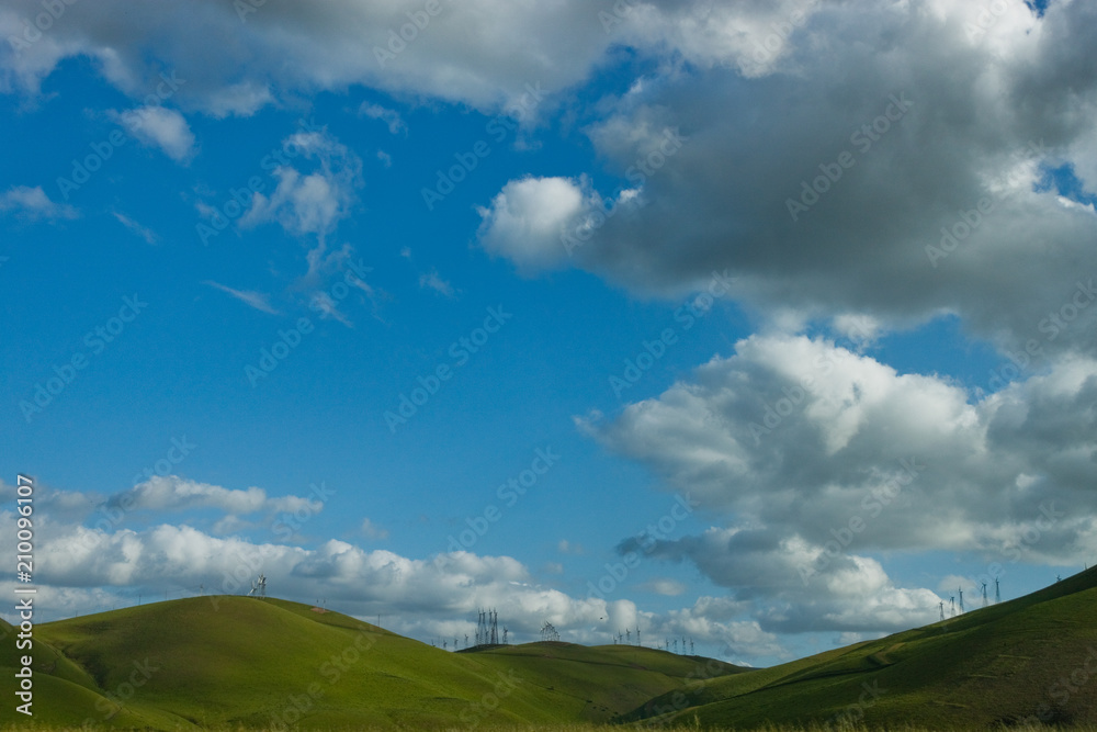 Cloudy Blue Sky With Green Rolling Hills & Windmills