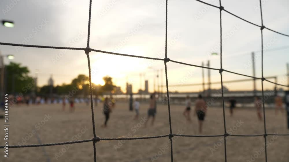 An extreme shallow depth of field slow motion view of people playing beach volleyball at the sand court on Pier 25 in Manhattan at sunset.  	
