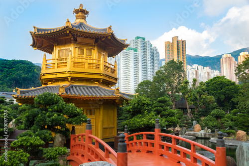 Golden Pagoda in Nan Lian garden  with red bridge and surrounded by green plants. The Hong Kong Skyline is in the background.