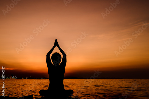 Silhouette meditating yoga woman practice on the beach in sunset background