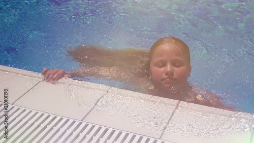 Pretty little girl with long blonde hair swiimming in the pool, closeup photo