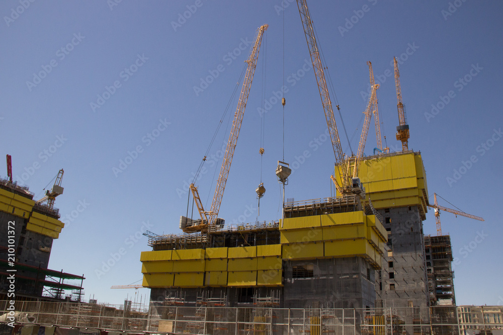 Construction of a modern high-rise building with cranes against the sky in summer
