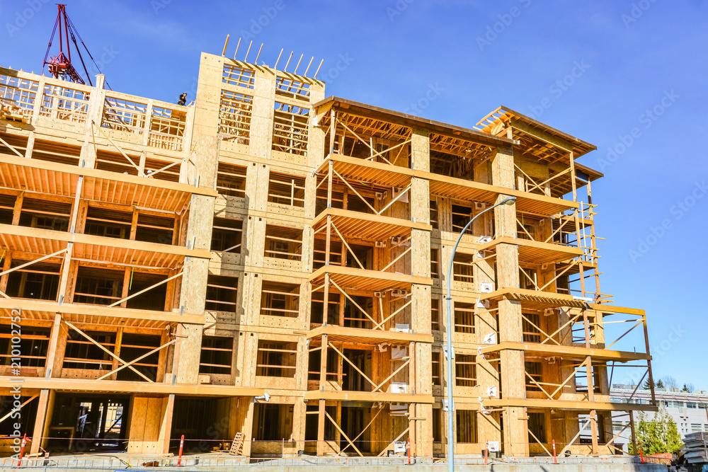 Six storey frame building under construction on concrete foundation bed on blue sky background