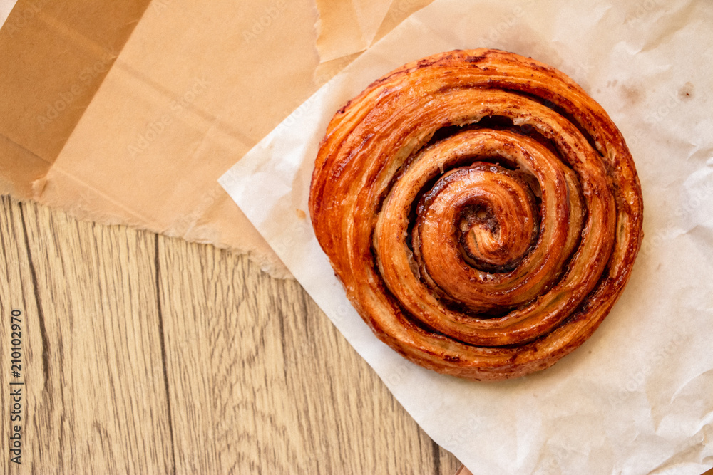 Fototapeta premium A baked cinnamon roll on white and brown paper. The close-up food photo.